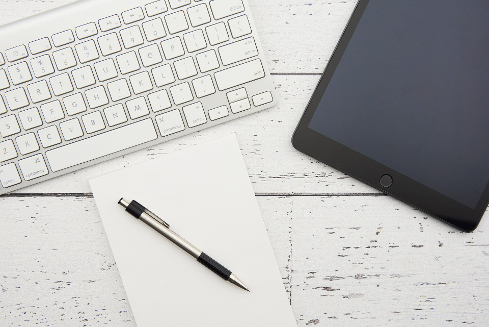 Keyboard, tablet and paper on a white wooden desk