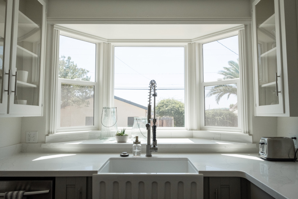Sink beneath a bay window in a white kitchen